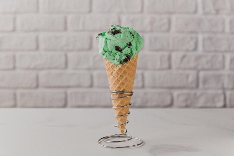 An ice cream cone with a single scoop of mint ice cream with chocolate cookie pieces in a spiral-shaped cone holder.