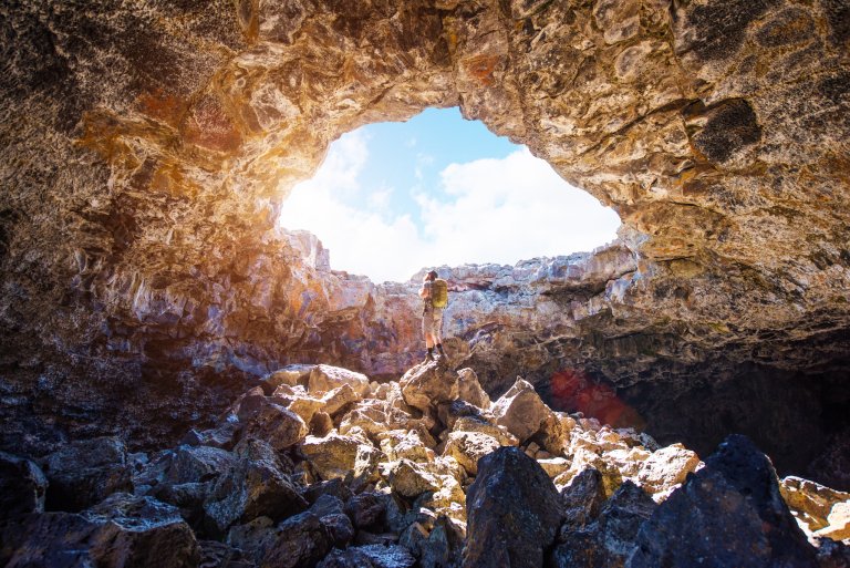 A person standing inside a cave, looking up at a natural skylight at Craters of the Moon National Monument & Preserve.