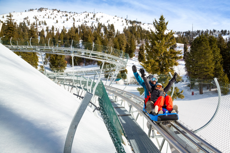 Two people riding the Glade Runner mountain coaster surrounded by trees and snowy landscapes at Bogus Basin.